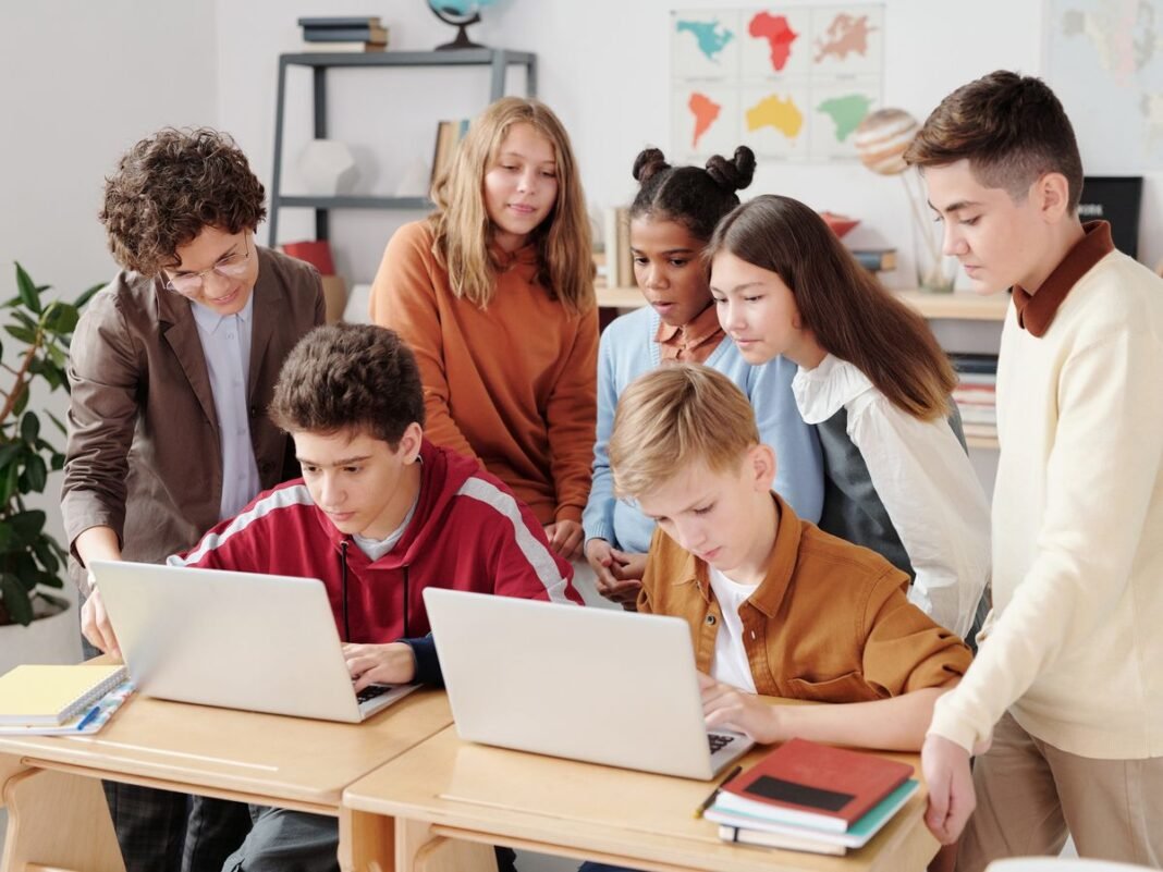 Teacher assisting students working together at classroom laptops