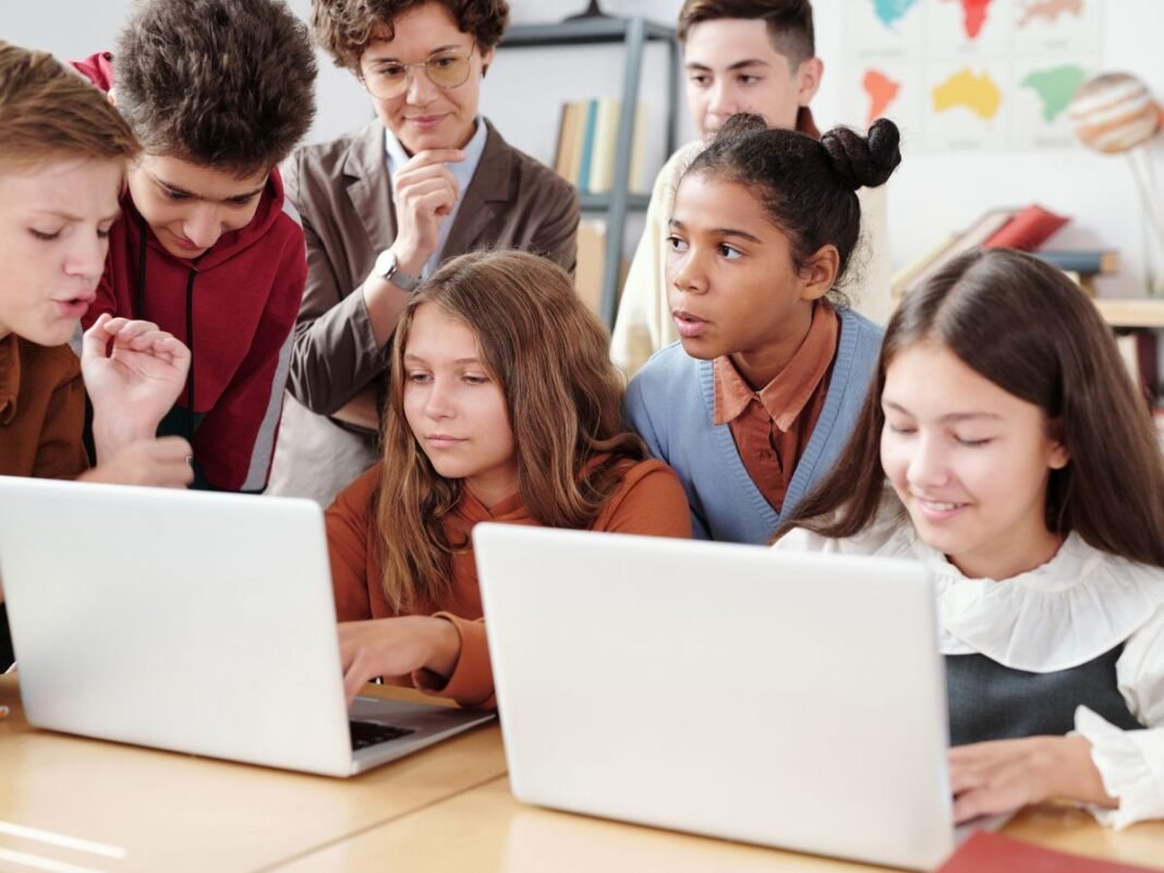 Students using laptops together in a classroom with a teacher
